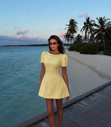 Female model wearing the Pastel Yellow Dress on a tropical seaside walkway