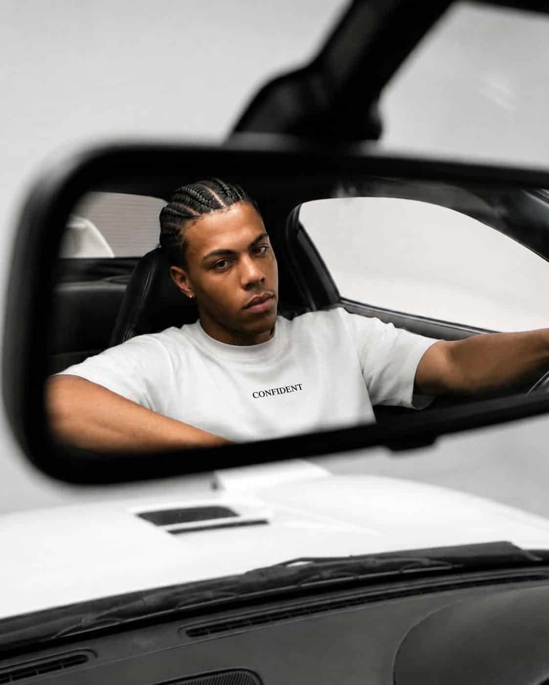 Man wearing a white S&A Collection CONFIDENT T-shirt reflected in a car mirror