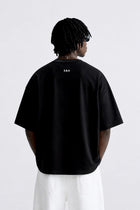 Back view of a male model wearing the black CONFIDENT oversized T-shirt with white trousers