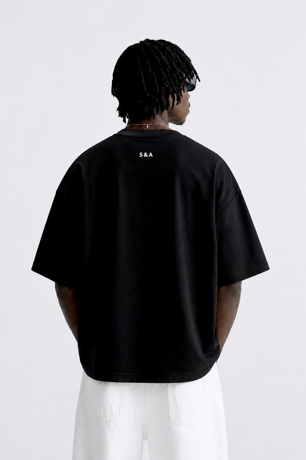Back view of a male model wearing the black CONFIDENT oversized T-shirt with white trousers