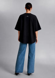 Back view of a female model wearing the black CONFIDENT oversized T-shirt with wide-leg jeans