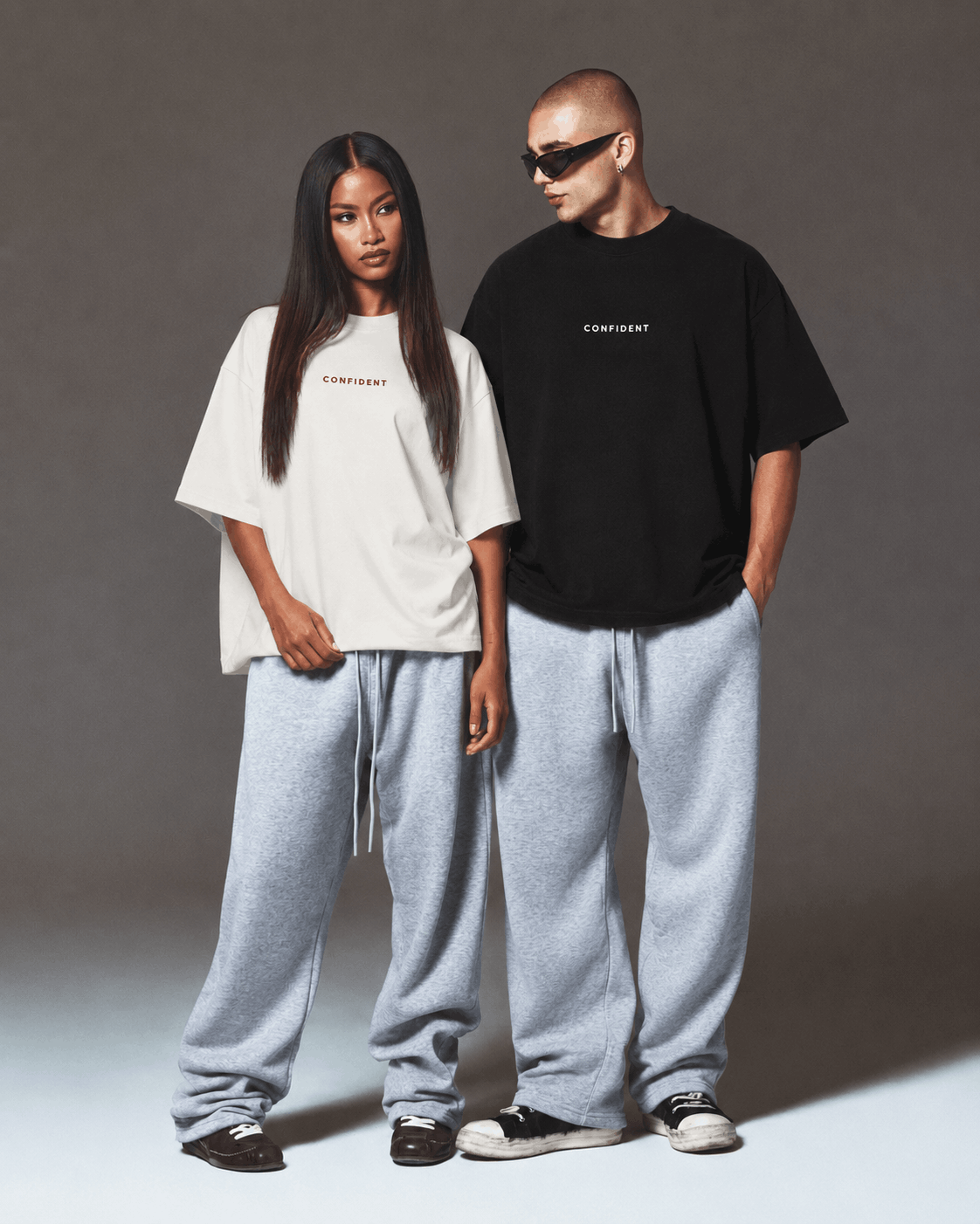 Female and male models wearing black and white CONFIDENT oversized T-shirts with grey sweatpants