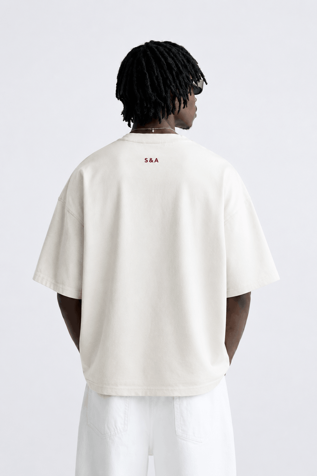 Back view of a male model wearing the white CONFIDENT oversized T-shirt with white trousers