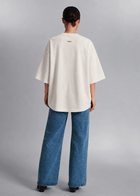 Back view of a female model wearing the white CONFIDENT oversized T-shirt with wide-leg jeans