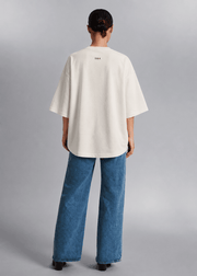 Back view of a female model wearing the white CONFIDENT oversized T-shirt with wide-leg jeans