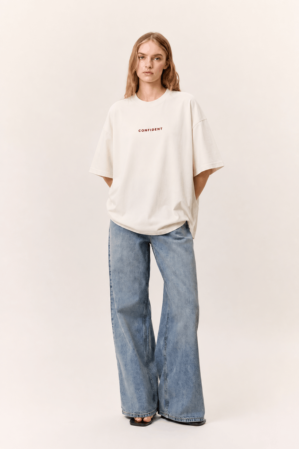 Female model wearing the white CONFIDENT oversized T-shirt with wide-leg jeans