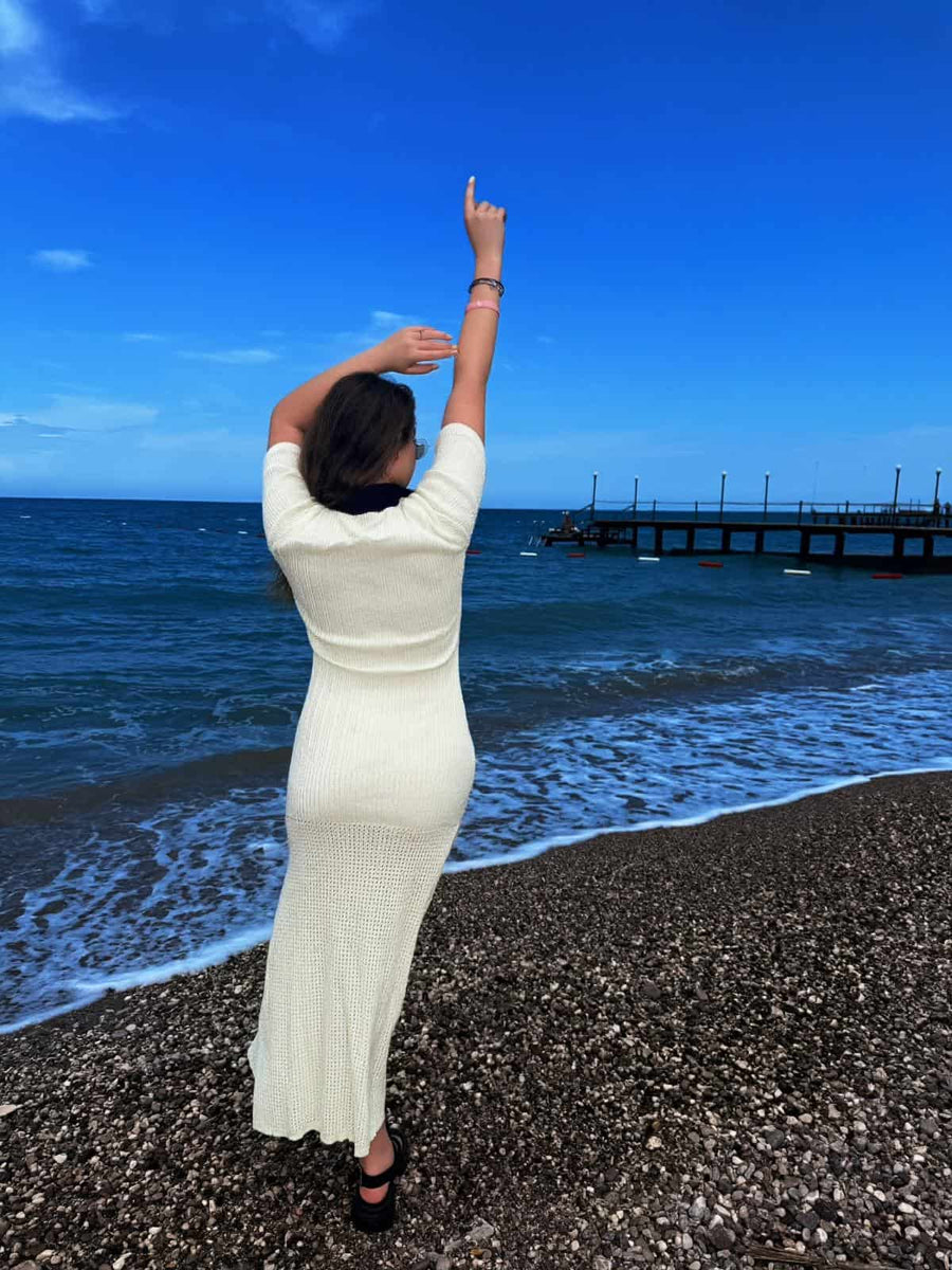 Back view of a female model wearing a cream crochet maxi dress by the sea