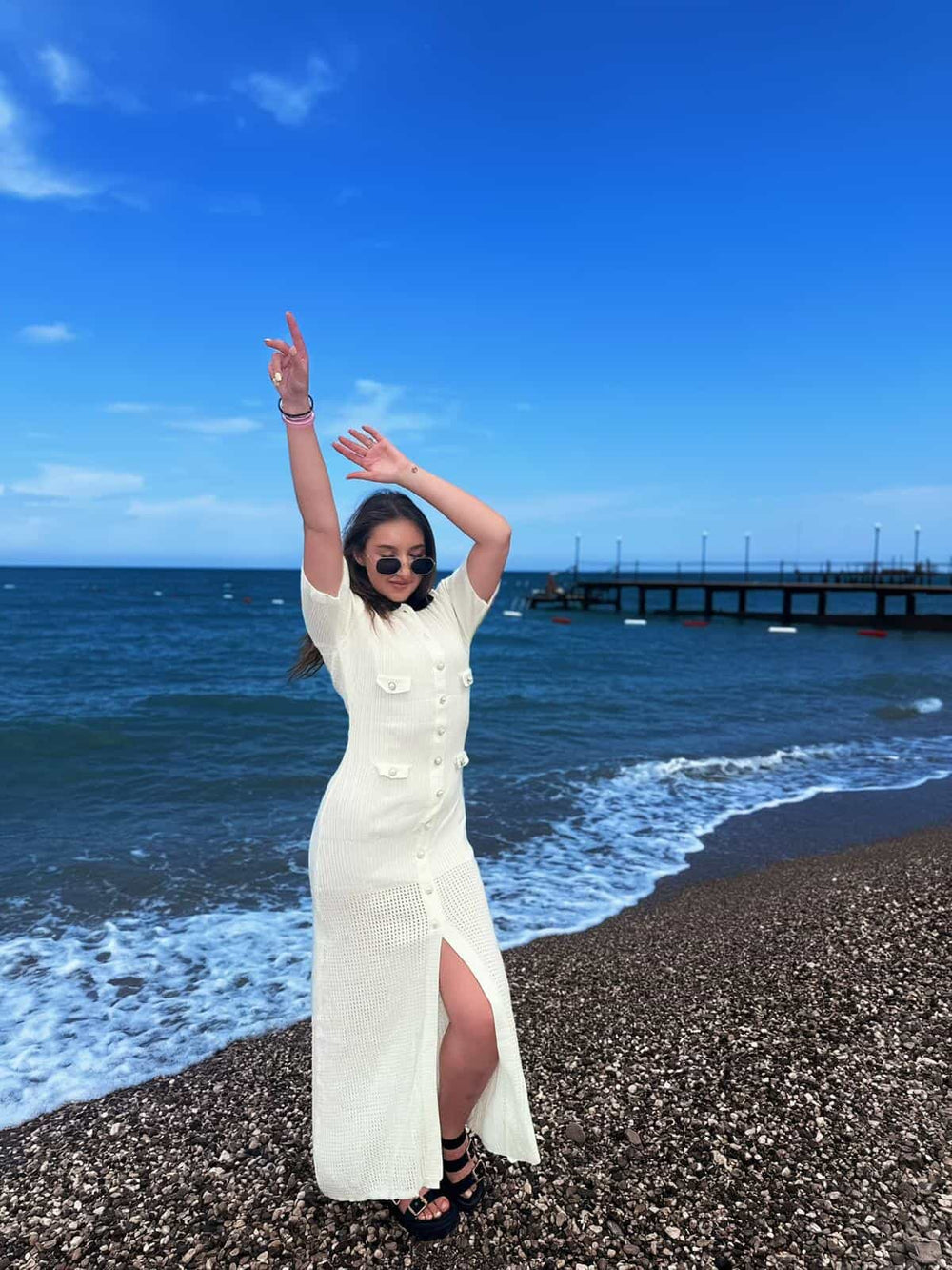 Female model wearing a cream crochet maxi dress on a pebble beach