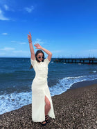 Female model wearing a cream crochet maxi dress on a pebble beach