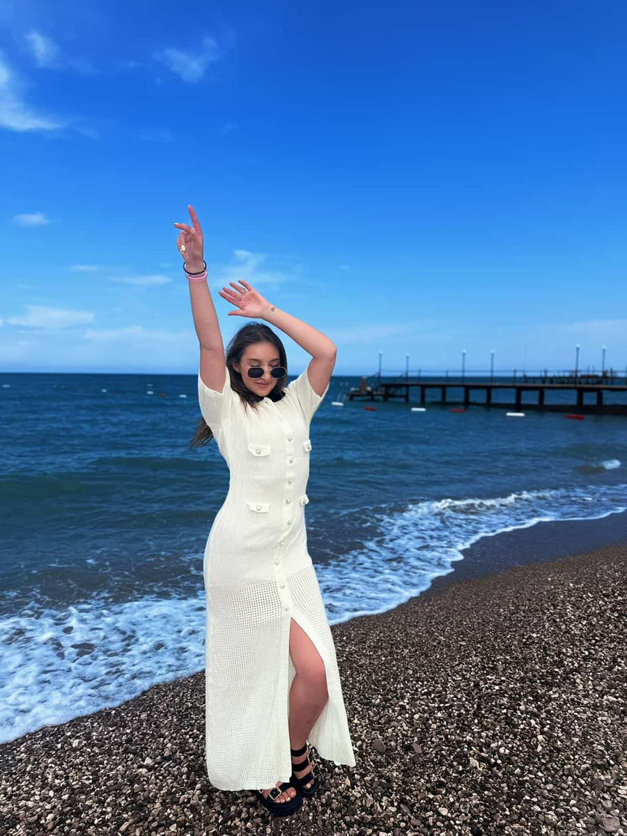 Female model wearing a cream crochet maxi dress on a pebble beach