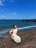 Female model seated on a pebble beach wearing a cream crochet maxi dress