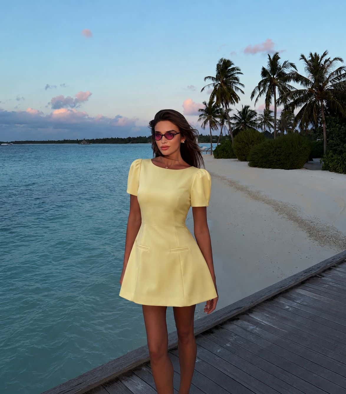 Female model wearing the Pastel Yellow Dress on a tropical seaside walkway